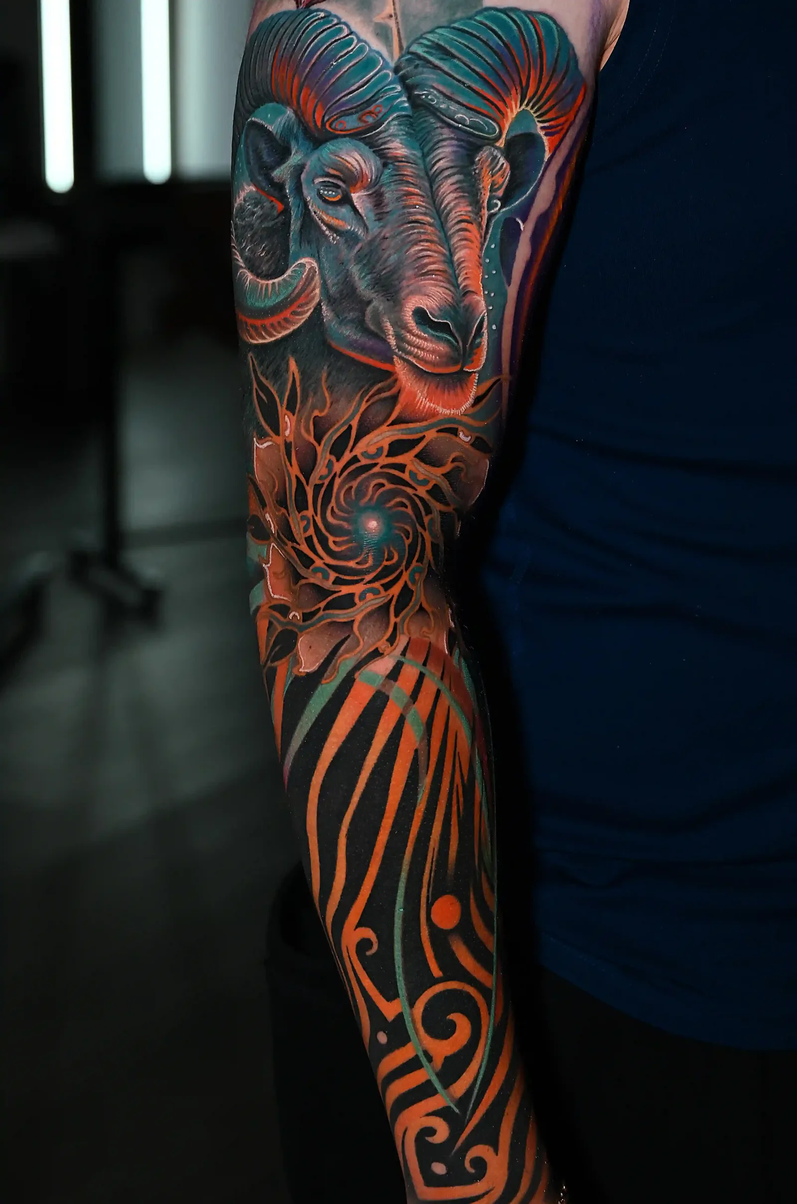 Color realism full sleeve of a glowing-eyed ram skull with ornamental linework by Danyi at Shadow Studio Charlotte