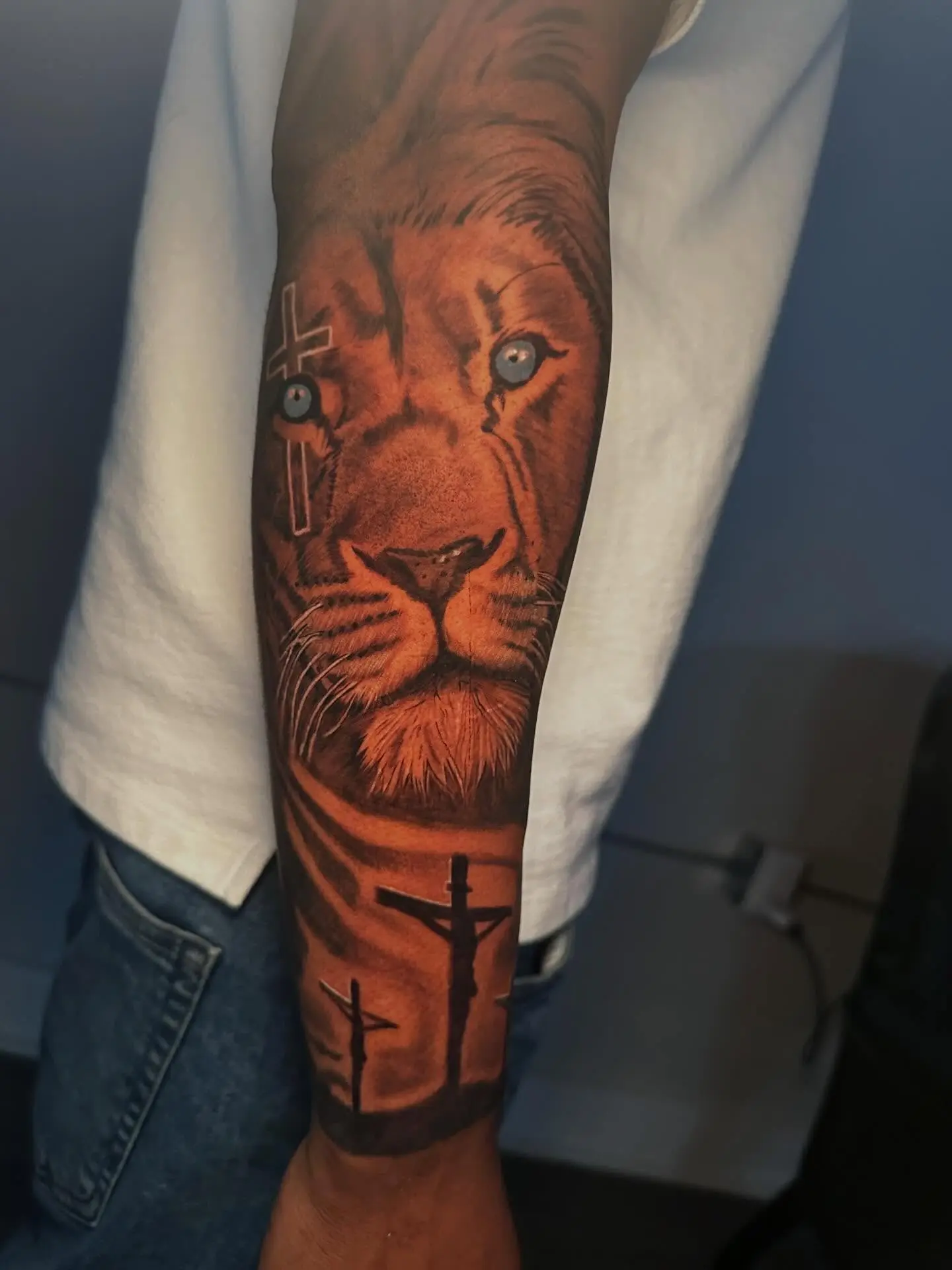 Color forearm tattoo of a lion portrait above a Calvary scene by Gynmo at Shadow Studio Charlotte
