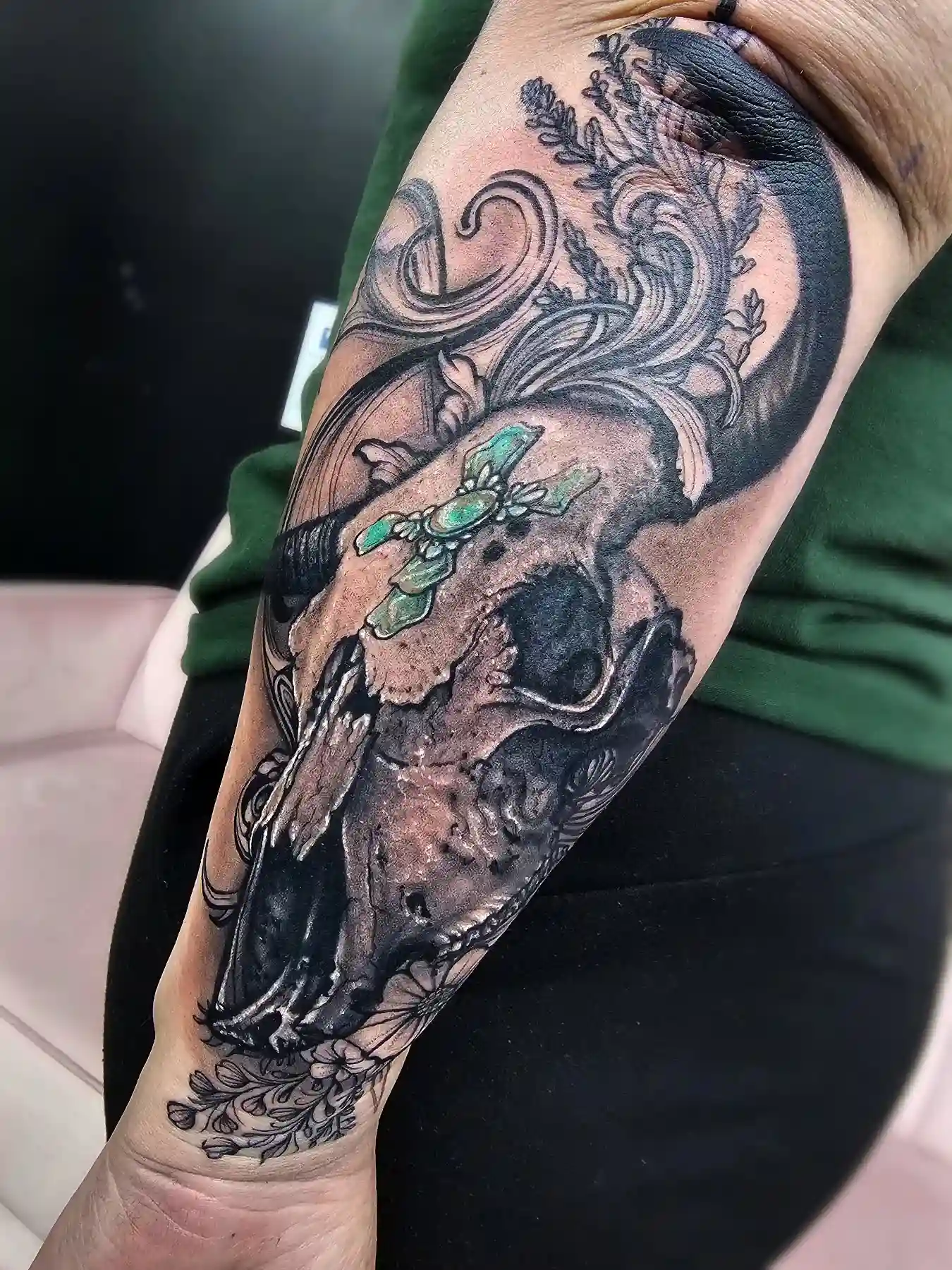 Black and grey neo-traditional bull skull with green gem and ornamental filigree on the forearm by Joel at Shadow Studio Charlotte