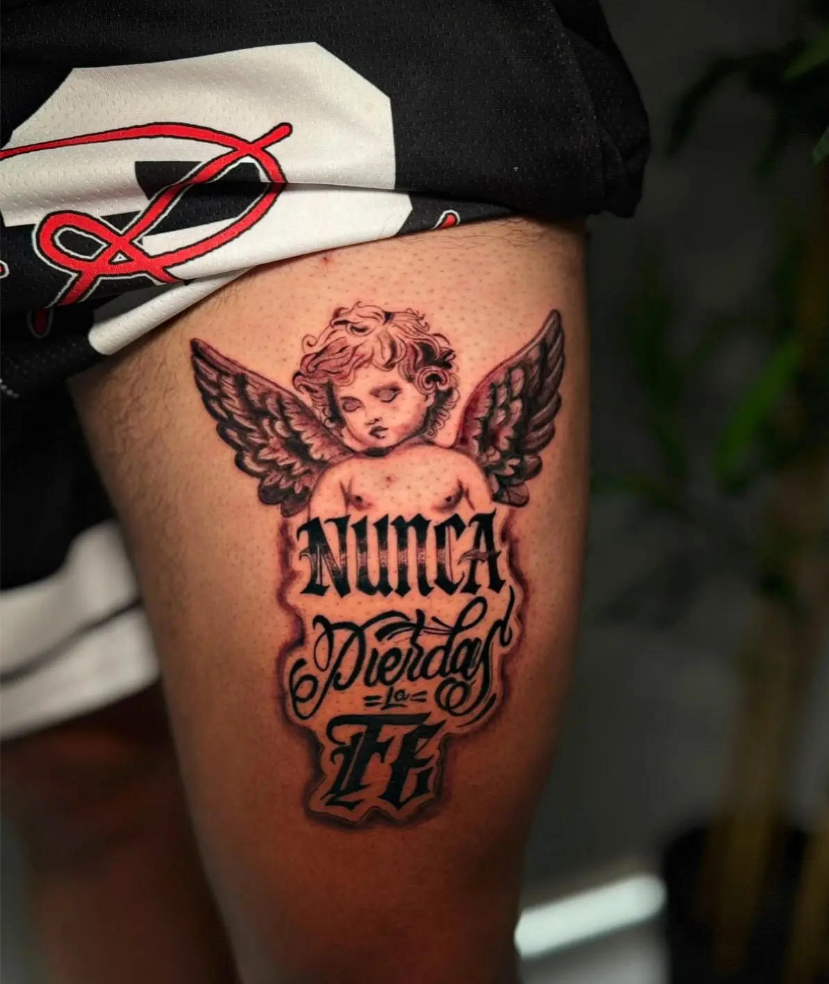 Black and grey thigh tattoo of a cherub above ornate lettering reading "Nunca Pierdas la Fe" by Venus at Shadow Studio Charlotte